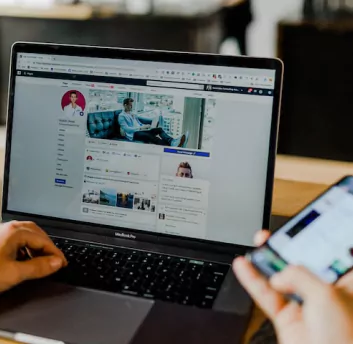 Image of person holding phone in one hand and on other hand working on laptop